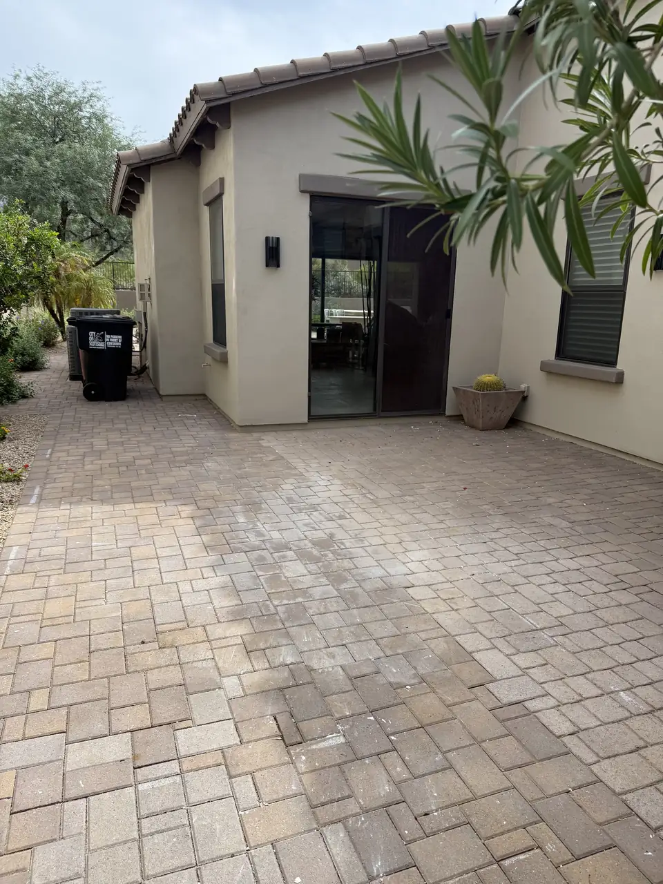 Clean brick paver patio beside a stucco house with a sliding glass door and a potted cactus, with nothing left on it