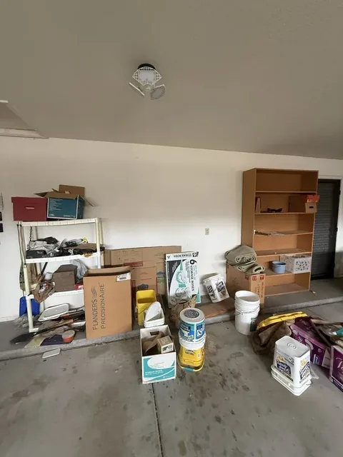 Garage floor and wall with buckets, cardboard boxes, a wire shelf, and a wooden bookcase gathered for removal