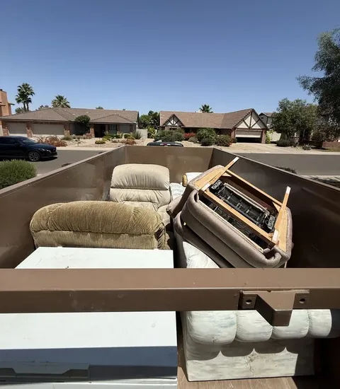 Dump trailer loaded with a loveseat, a recliner, a refrigerator and a sofa on a residential street