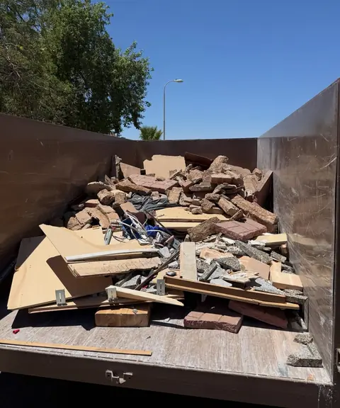 Dump trailer loaded with broken brick, plywood and lumber scraps under a clear blue sky